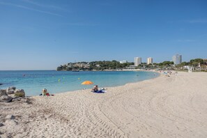 A beach with a clear sky, sandy shore, and buildings in the background.
