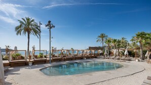A pool area with lounge chairs and umbrellas, surrounded by palm trees and a clear sky.