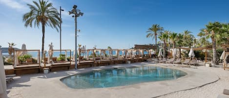 A pool area with lounge chairs and umbrellas, surrounded by palm trees and a clear sky.