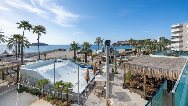 A resort with a pool, beach, palm trees, and a view of the sea.