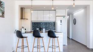 A modern kitchen with white cabinets, a black backsplash, and three black bar stools.