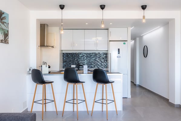 A modern kitchen with white cabinets, a black backsplash, and three black bar stools.