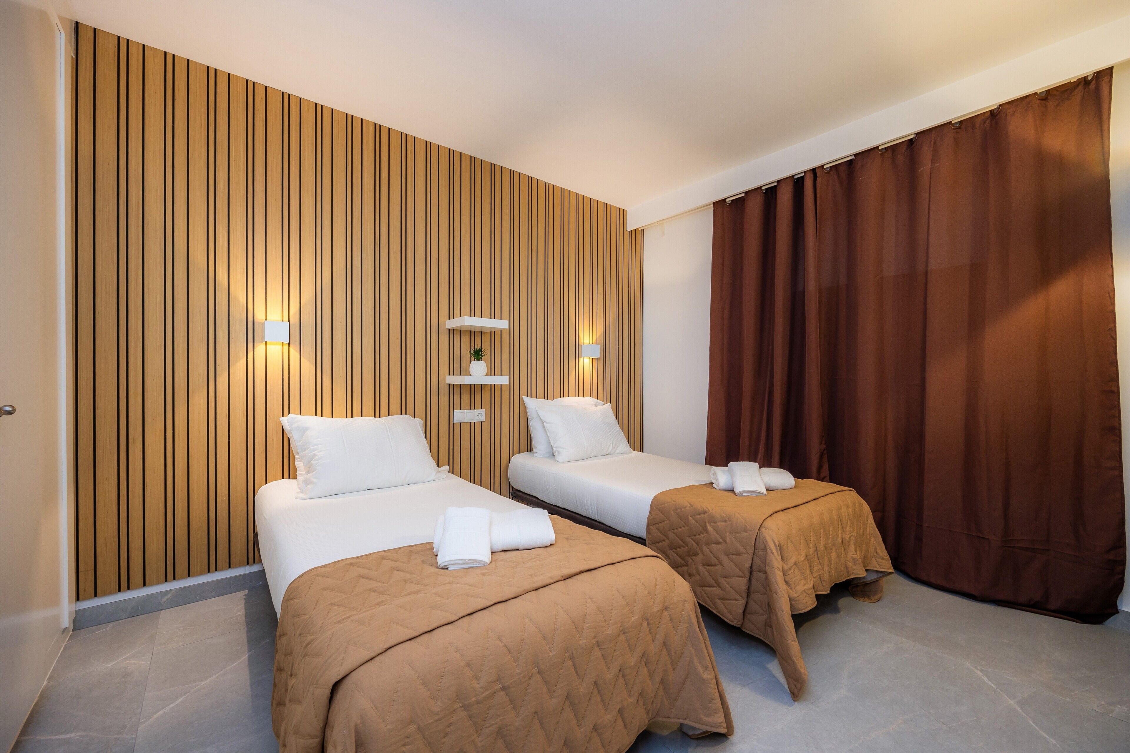 Habitación de hotel con dos camas, paneles de madera en la pared, un estante con una planta y una cortina marrón.
