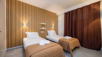 Habitación de hotel con dos camas, paneles de madera en la pared, un estante con una planta y una cortina marrón.