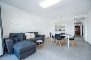 Una sala moderna con un sofá seccional gris, una mesa de comedor con sillas y una pequeña mesa redonda.