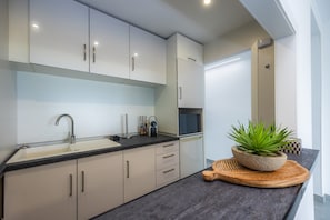 A modern kitchen with white cabinets, a black countertop, a sink, a microwave, and a potted plant. - First Line Mediterranean Apartment with Sea Views, Wi-Fi and Air Conditioning (Calvià)