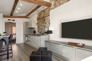 A modern kitchen with a stone accent wall, a dining area with stools, and a large flat-screen TV mounted on the wall.
