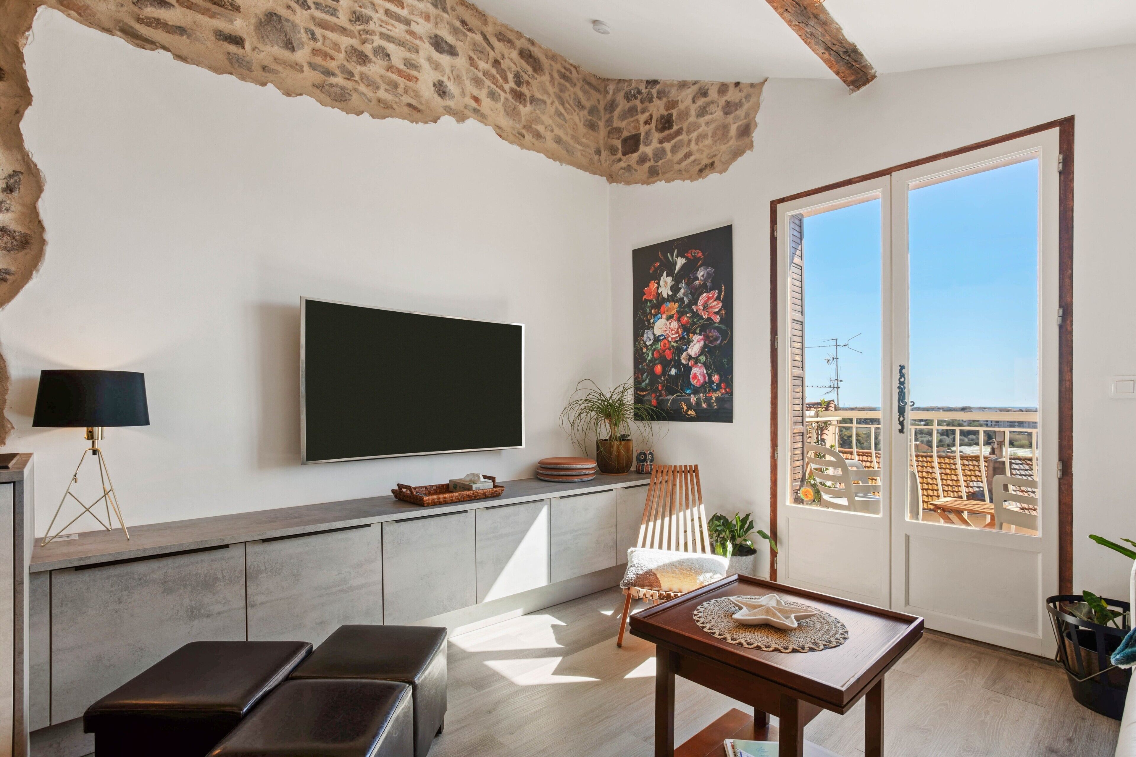 Una sala de estar moderna con una televisión de pantalla plana, una mesa de comedor, un banco y un balcón con vistas.