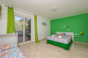 Un dormitorio con cama, escritorio, pared verde y puerta corredera de vidrio al exterior.