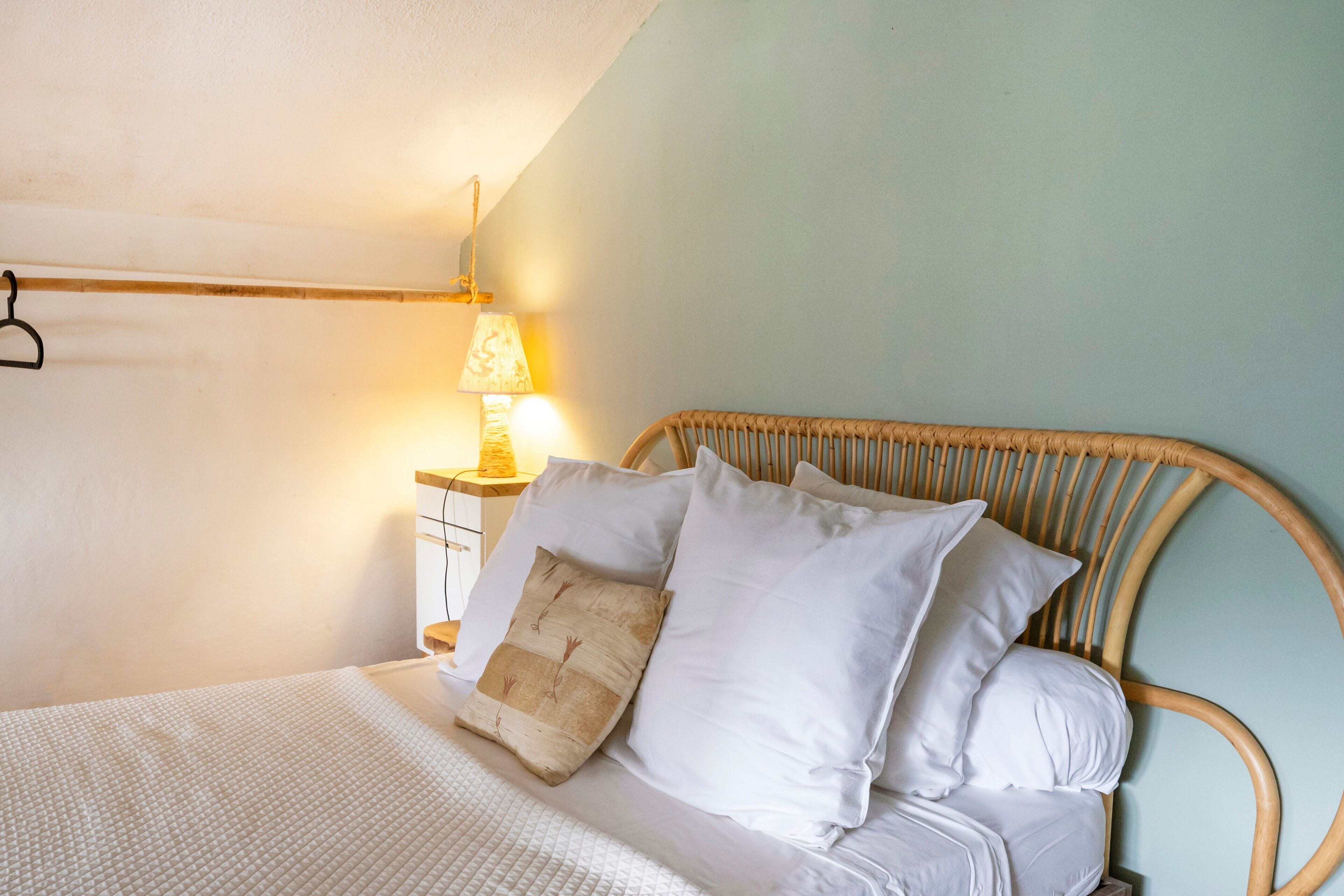 Una cama con ropa blanca, cabecera de madera y lámpara de noche.