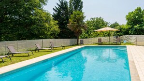 A rectangular swimming pool with a tiled edge, surrounded by a grassy area with lounge chairs and a palm tree. - Cottage 'La Caseta' with Shared Pool, Wi-Fi and Air Conditioning (Panjas)