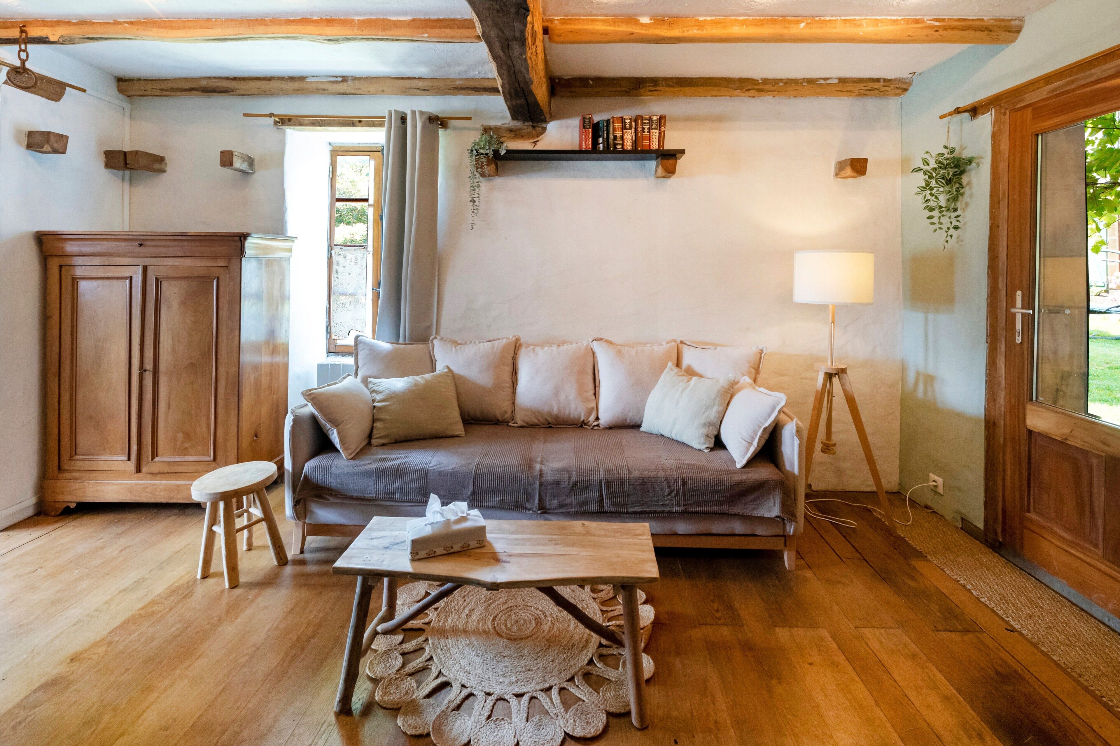 A cozy room with a wooden floor, a sofa with cushions, a small stool, a table with a placemat, a lamp, and a bookshelf. - Cottage 'La Caseta' with Shared Pool, Wi-Fi and Air Conditioning (Panjas)