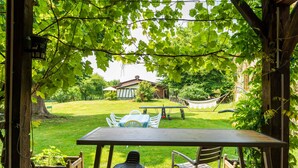 A wooden pergola with a table and chairs, a hammock, and a grassy yard with a house in the background. - Cottage 'La Caseta' with Shared Pool, Wi-Fi and Air Conditioning (Panjas)
