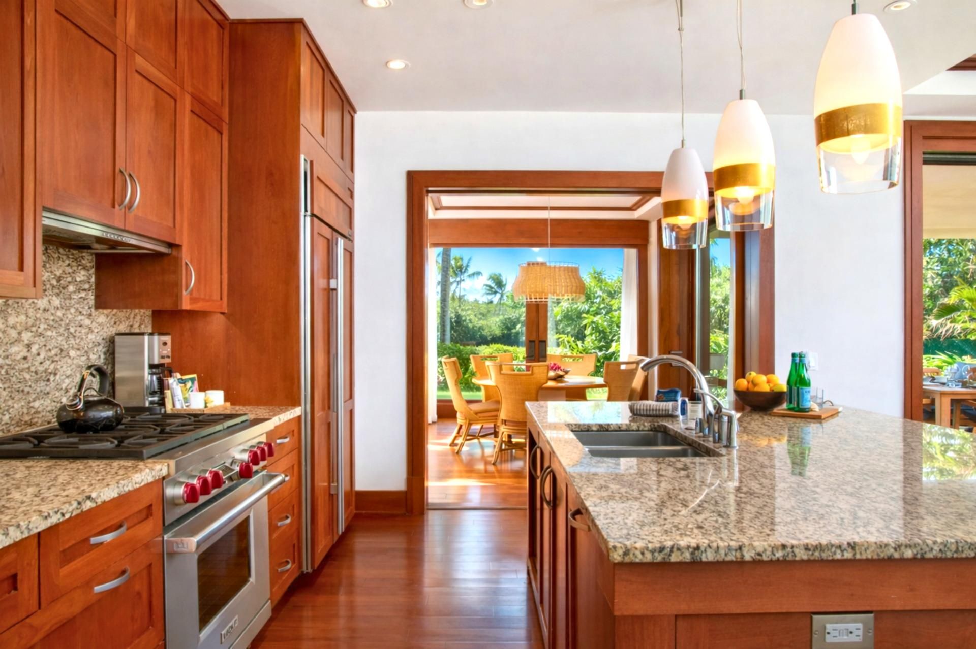 Eine moderne Küche mit Holzschränken, Granit Arbeitsplatten, Edelstahlgeräten und Pendelleuchten.