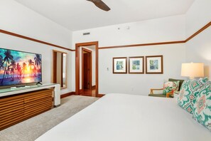 Ein Hotelzimmer mit Bett, Fernseher, Schreibtisch, Stuhl, Lampe und gerahmten Bildern an der Wand.
