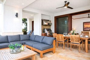 Ein modernes Wohnzimmer mit Ecksofa, Esstisch aus Holz, Stühlen und Deckenventilator.