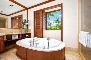 Ein Badezimmer mit einer großen Badewanne, Holzklappläden, einem Waschtisch mit Spiegel und Blick auf Palmen durch ein Fenster.