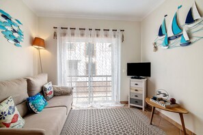 A living room with a sofa, a coffee table, a TV stand, and a window with curtains.