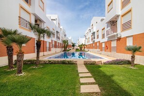 A modern building with a central swimming pool, surrounded by well-maintained grass and palm trees.
