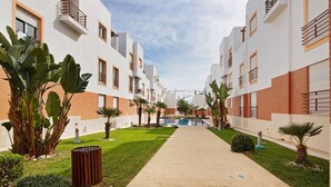 Un chemin menant à un bâtiment doté de nombreux balcons, entouré de verdure et sous un ciel dégagé.