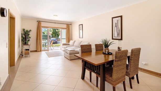 A dining area with a wooden table and wicker chairs, a sofa, and a potted plant.