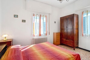 A bedroom with a bed, a wooden wardrobe, a radiator, and a window with curtains.