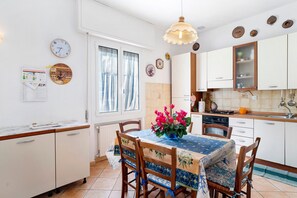 A kitchen with white cabinets, a dining table with chairs, a hanging light fixture, and a window with curtains.