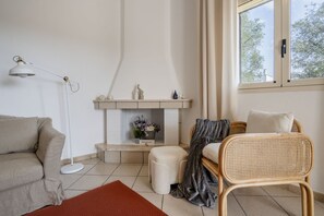 Ein Wohnzimmer mit einer Couch, einem Sessel, einer Stehlampe, einem Kamin und einem Fenster mit Vorhängen.