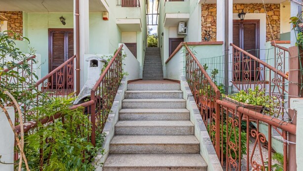 Una escalera que lleva a un edificio con balcones, rodeado de follaje.