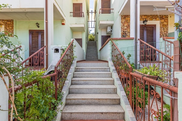 A staircase leading to a building with balconies, surrounded by greenery.