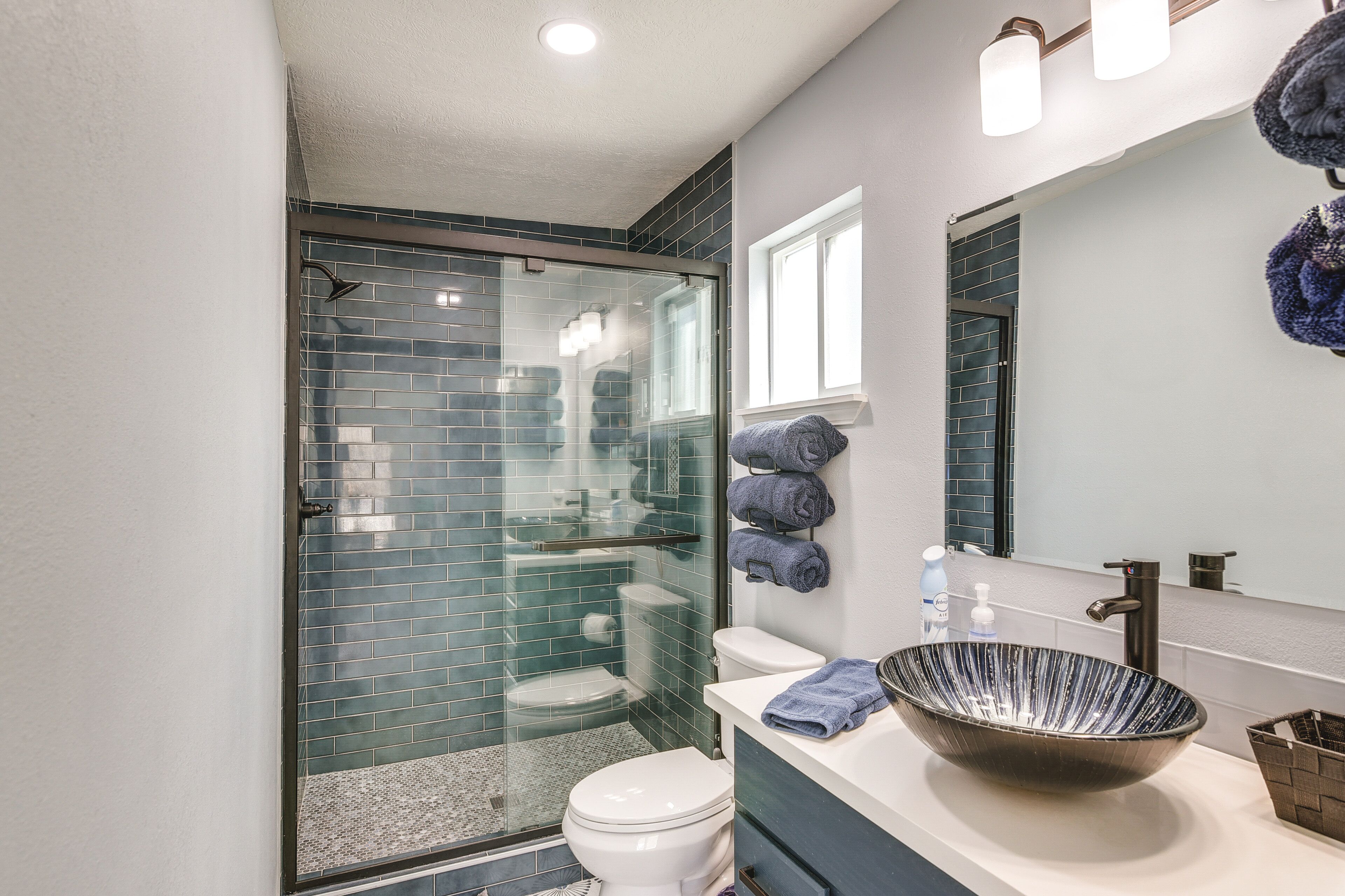 A bathroom with a glass-enclosed shower, a white toilet, a large vessel sink, and a mirror with a towel rack.