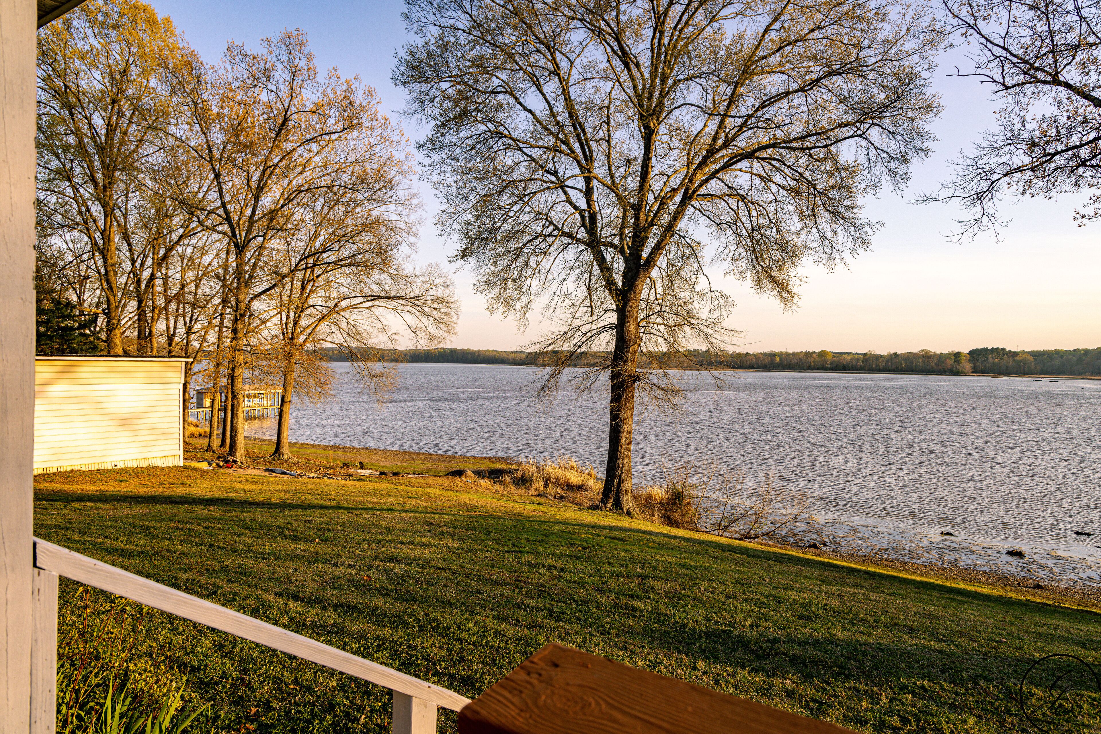 A lakeside view from a covered deck with a grassy area and trees.
