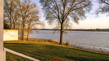 A lakeside view from a covered deck with a grassy area and trees.
