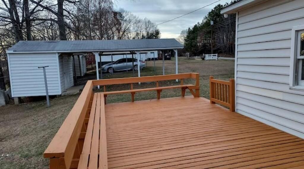 Eine Holzterrasse mit einer Bank, einem kleinen Schuppen und einem Auto im Hintergrund.