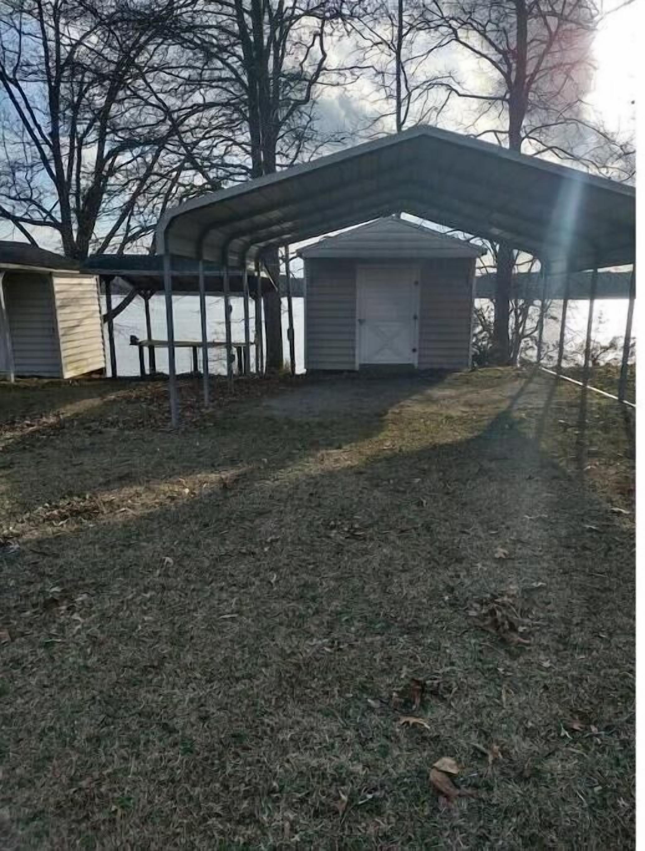 A covered outdoor area with a metal roof, a small shed, and a grassy ground.
