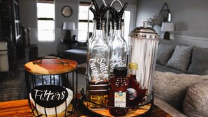 Ein Holztisch mit einem schwarz-weißen Schild mit der Aufschrift 'Filters', einer Glas-Kanne mit der Bezeichnung 'Irish Caramel' und einer Glasflasche mit dem Etikett 'Light Amber Mountain Forest'.