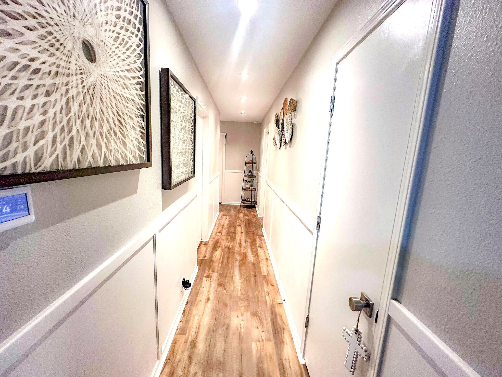 Un pasillo estrecho con piso de madera, paredes blancas y una puerta a la derecha.