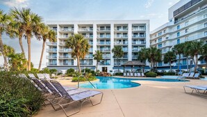 Un hotel con zona de piscina, palmeras y un edificio de varios pisos con balcones.