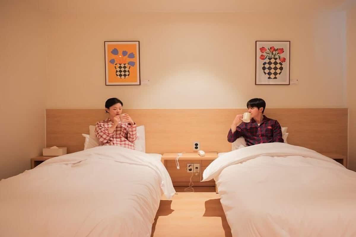 Une chambre d’hôtel avec deux lits, une table de chevet avec une lampe et deux œuvres d’art encadrées au mur.