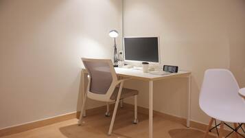 A minimalist office setup with a desk, two chairs, a computer monitor, a lamp, and a clock.