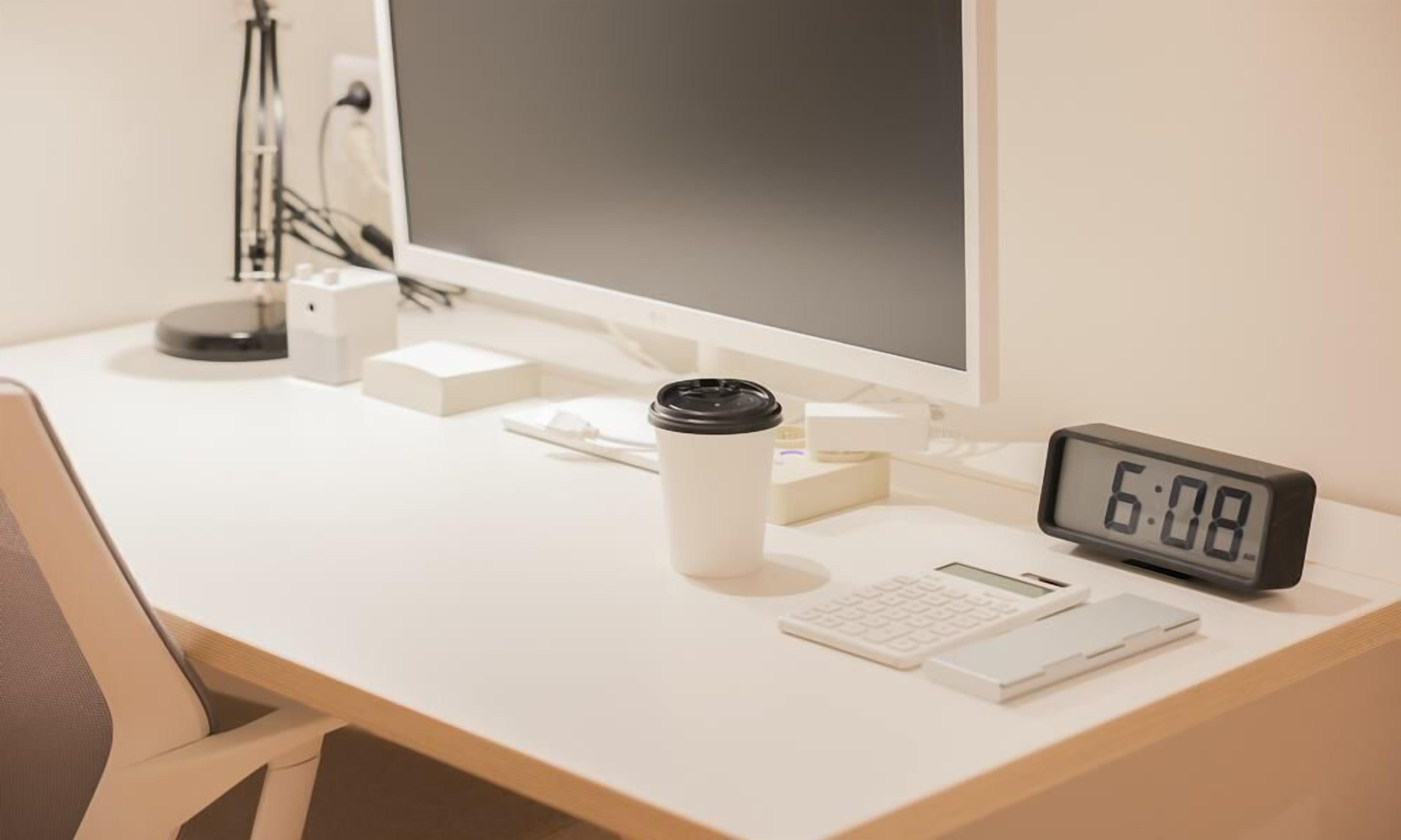 A desk with a computer monitor, a coffee cup, a keyboard, a mouse, and a digital clock displaying 6:08.