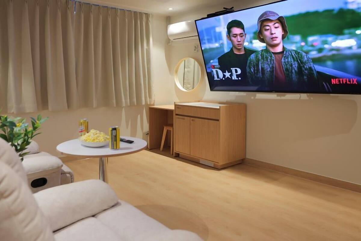 Un salon moderne avec un téléviseur à écran plat, une table ronde sur laquelle sont disposés des en-cas, un canapé et un meuble en bois.