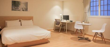 A hotel room with a bed, a desk, a chair, a small table, and a window with curtains.