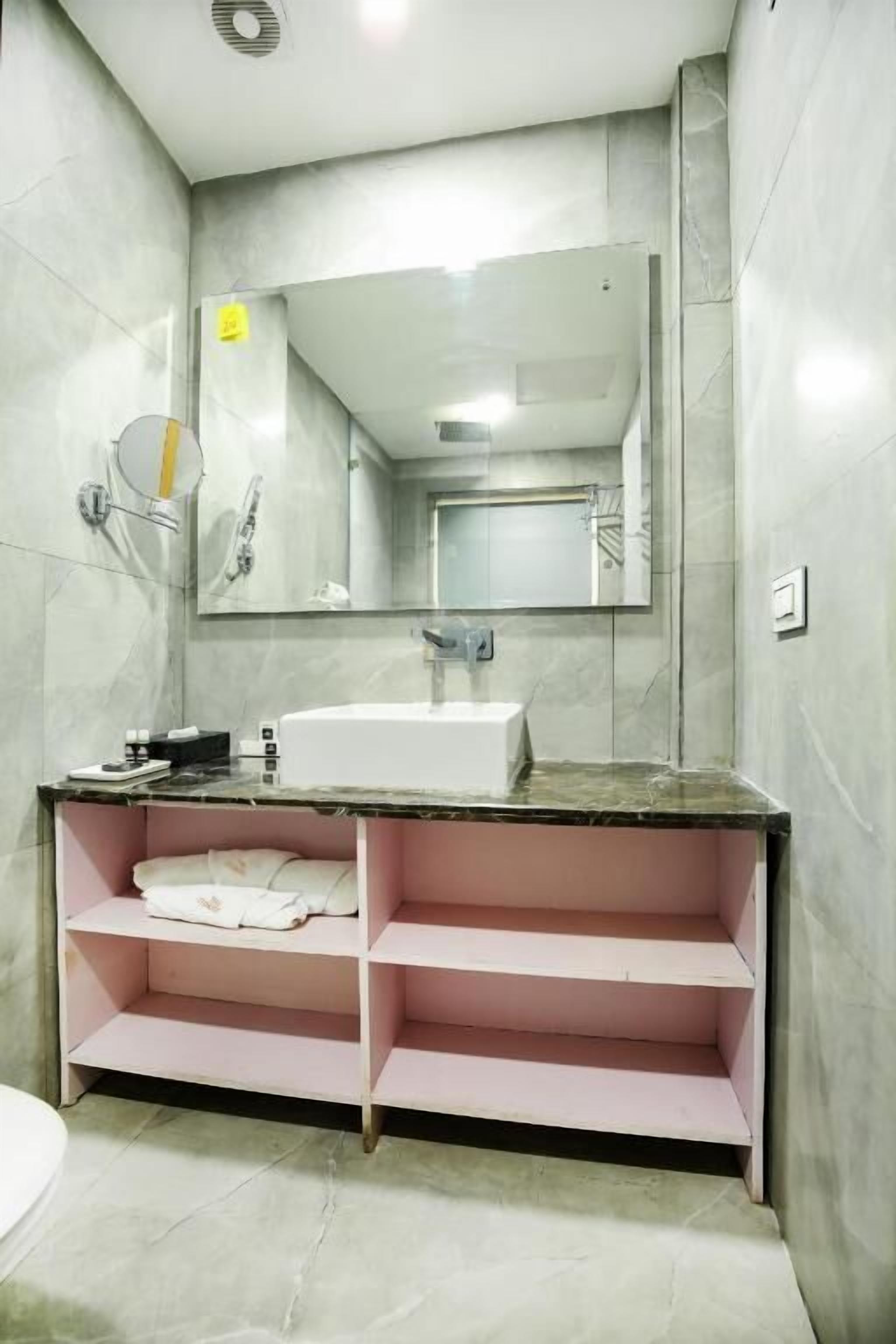 Un baño con un lavamanos blanco, un espejo y un estante rosa.