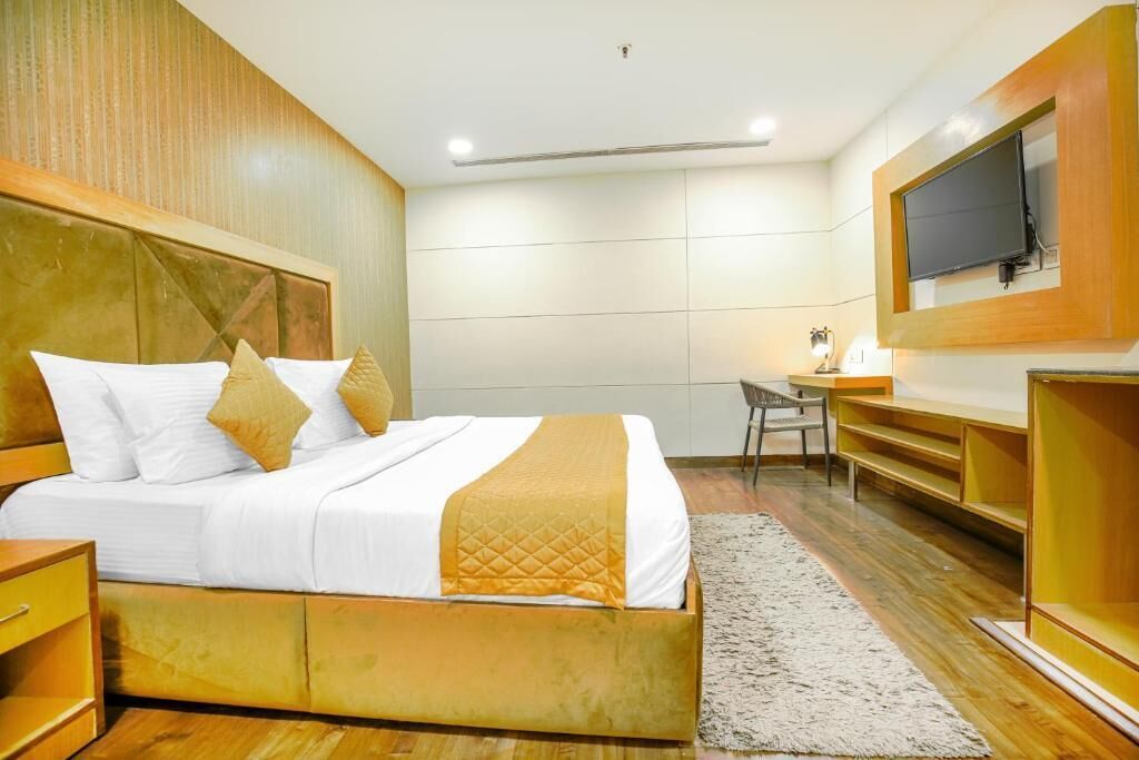 Un dormitorio moderno con una cama grande, cabecera de madera, un escritorio y un televisor montado en la pared.