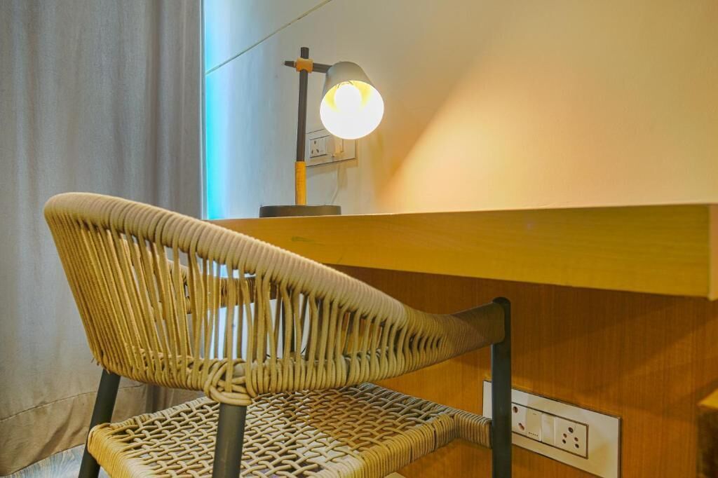 Una silla de mimbre con respaldo y asiento tejido, ubicada frente a una barra de madera con una lámpara de pared sobre ella.