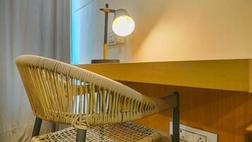 Una silla de mimbre con respaldo y asiento tejido, ubicada frente a una barra de madera con una lámpara de pared sobre ella.