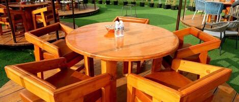 Una mesa redonda de madera con sillas, rodeada de plantas en macetas y mobiliario de exterior.