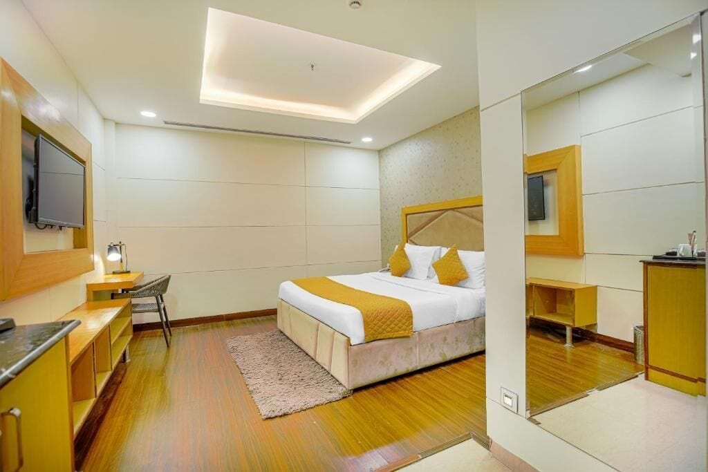 A hotel room with a bed, a desk, a chair, a television, and a mirror.