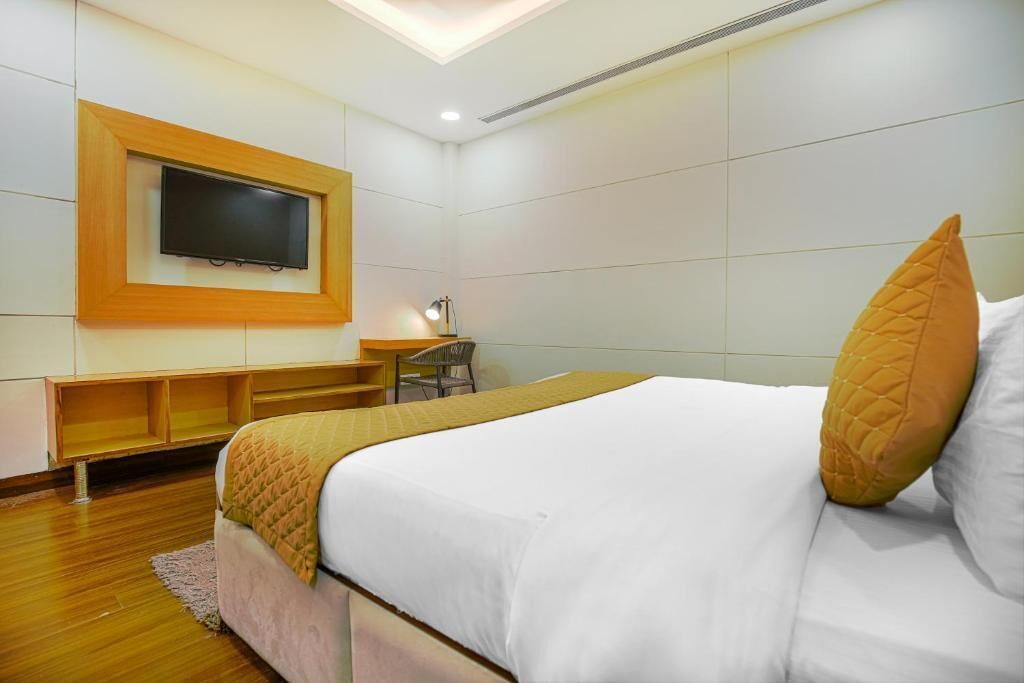 A hotel room with a bed, a desk, a chair, and a television mounted on the wall.